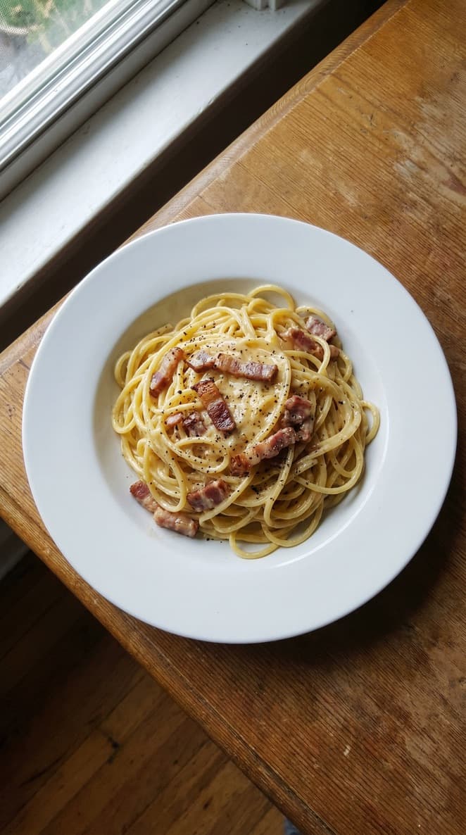 A bowl of carbonara pasta with black pepper and crispy pancetta