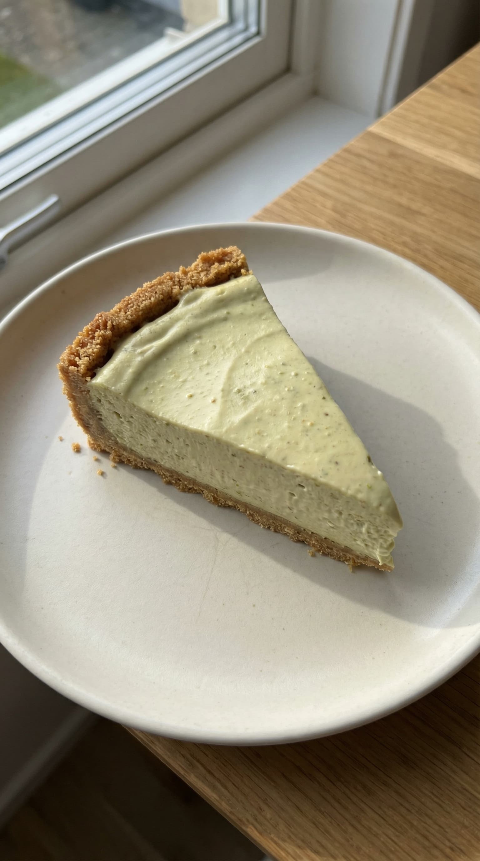 A creamy pistachio cheesecake topped with crushed pistachios on a plate.