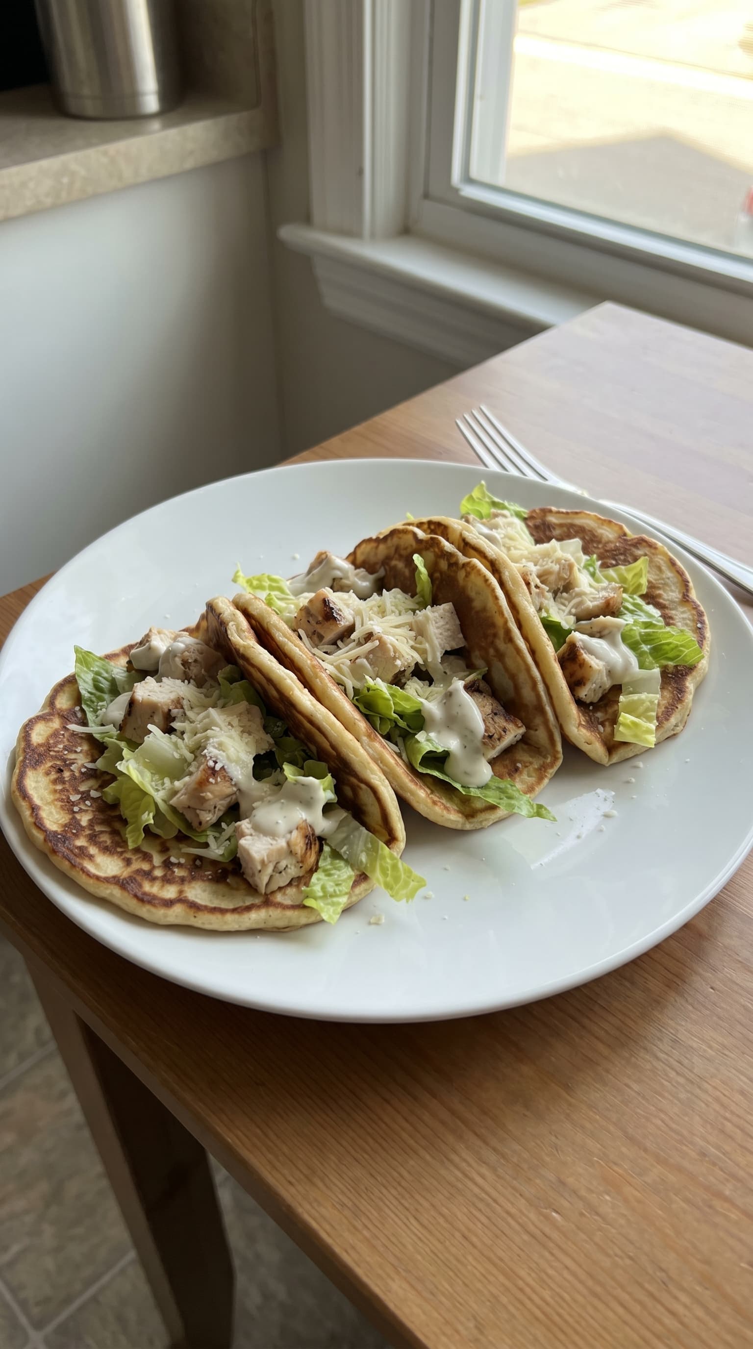Chicken Caesar pancake tacos on a white plate with golden savory pancakes, grilled chicken pieces, romaine lettuce, Caesar dressing, and Parmesan cheese.