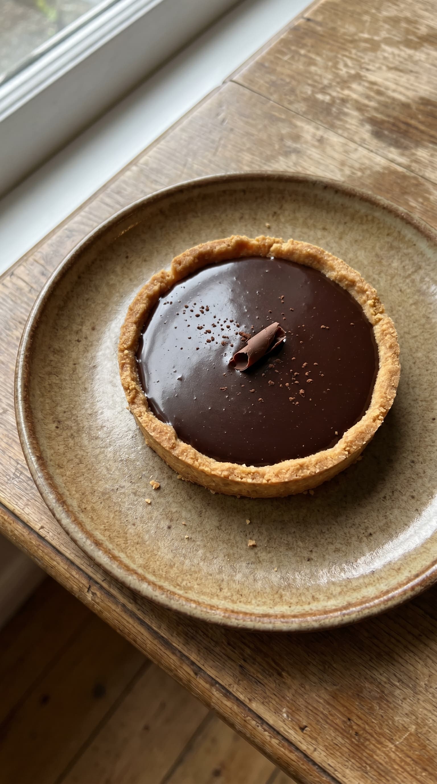 Chocolate tart on a plate with smooth ganache and a chocolate decoration.